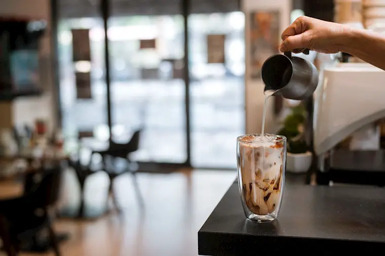 barista pouring milk into ice coffee background