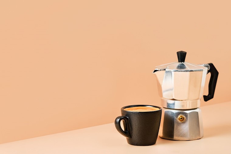 mug and coffee maker on pink table background